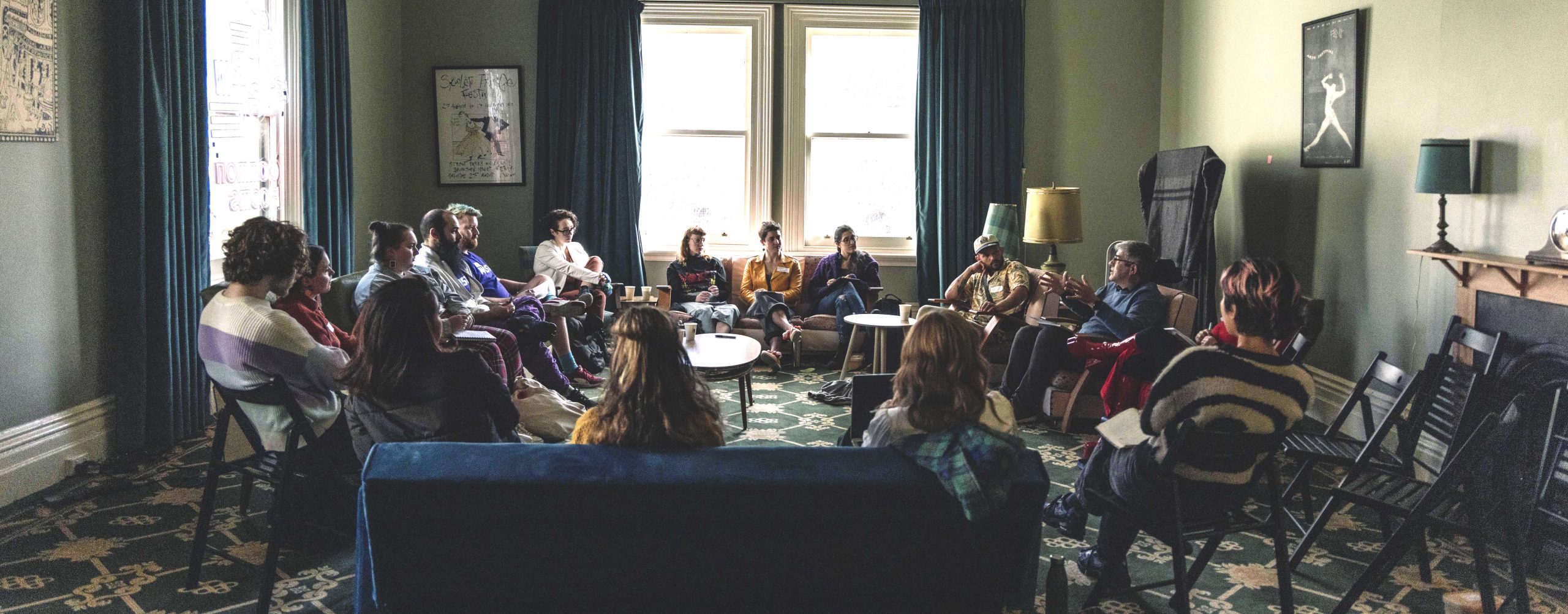An image of the circus and physical theatre breakout session at the TNA Producing Fundamentals event in July 2023. Attendees are sitting on couches and chairs in a circle facing inwards, listening to a guest speaking talk.